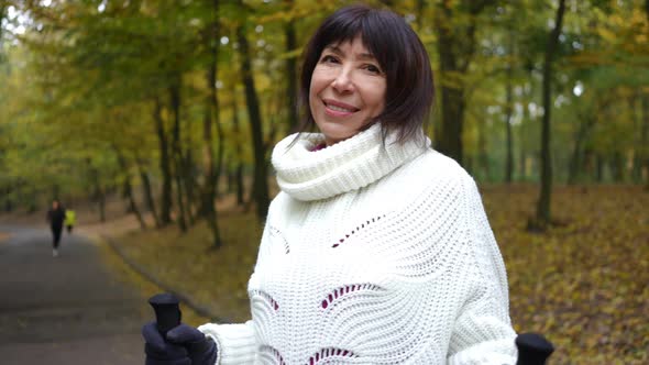 Happy Brunette Mature Woman with Brown Eyes Looking at Camera Smiling Standing with Poles for Nordic