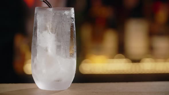 Limonade is Being Poured to the Ice Cube in Cocktail Glass on the Bar Counter in Slow Motion Full