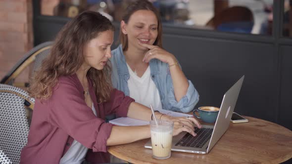 Happy Women Working Together with Laptop at Outdoor Cafe