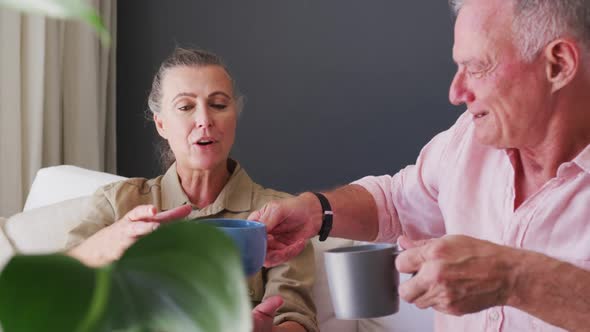 Caucasian senior couple holding coffee cup talking to each other while sitting on the couch at home