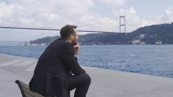 Thoughtful businessman sitting on bench by the sea in the city.