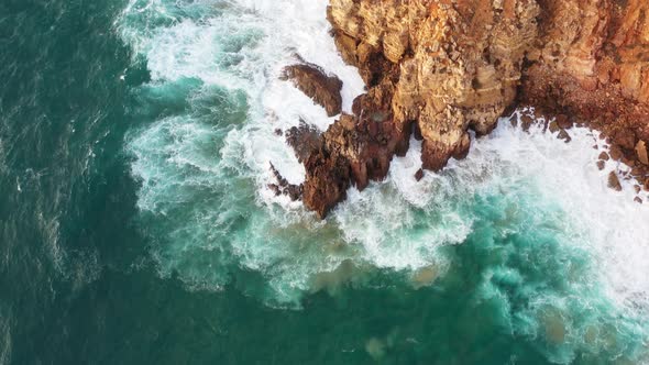 Rocky shore of Praia Do Tonel Portugal eroded cliffs splashed by ocean waves, Aerial lowering reveal