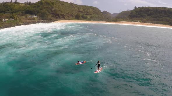 Aerial view of two men sup stand-up paddleboard surfing in Hawaii