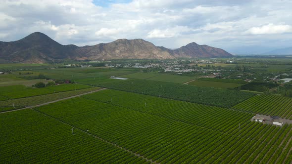 Aerial pan right of green farm fields, mountains in background, on a cloudy day, Cachapoal Valley, s