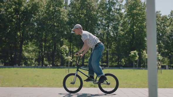 BMX Extreme Cyclist Rides Through the City Park and Performs Stunts