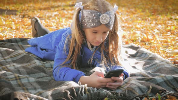 A Beautiful Teen Girl a Park During Golden Autumn Time and Uses Mobile Phone. Concept of Online