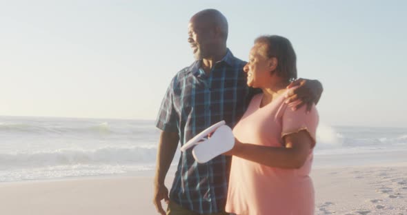 Smiling senior african american couple embracing and walking on sunny beach