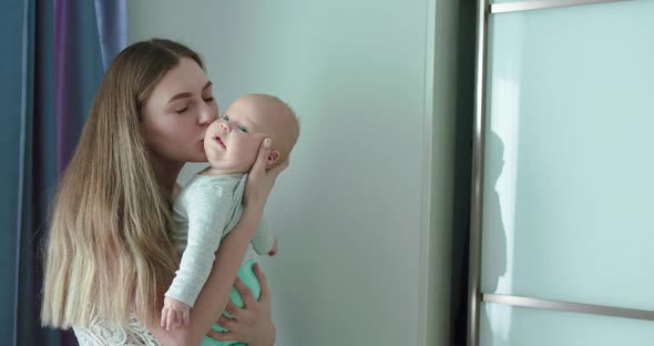 Happy Mother Holds Lovely Newborn Son Kisses Him and Rejoices in Room