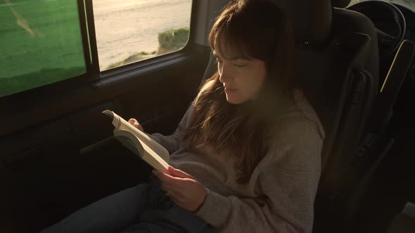 Traveling woman reading book in van at sunset