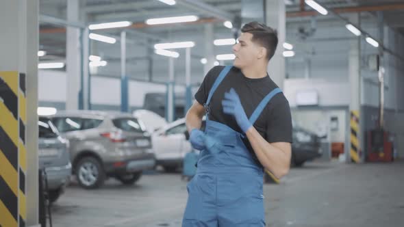 Positive Handsome Young Auto Mechanic in Uniform Dancing in Slow Motion in Repair Shop