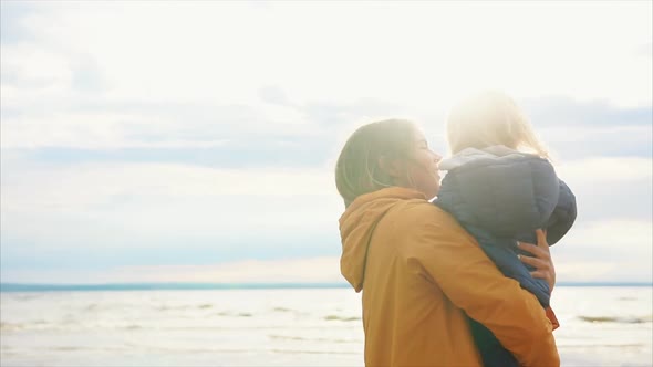 An Adult Mother Holds a Young Daughter Who Blows Soap Bubbles Near the Beach