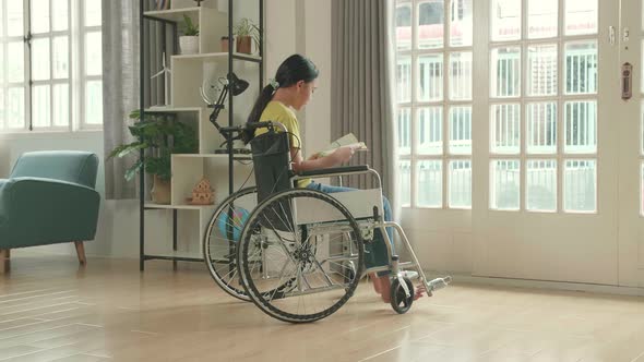 Asian Kid Girl Sitting In A Wheelchair Reading Book Near Door In The House