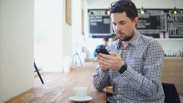 Man in Casual Wear Sitting in the Cafe. He Using His Smartphone