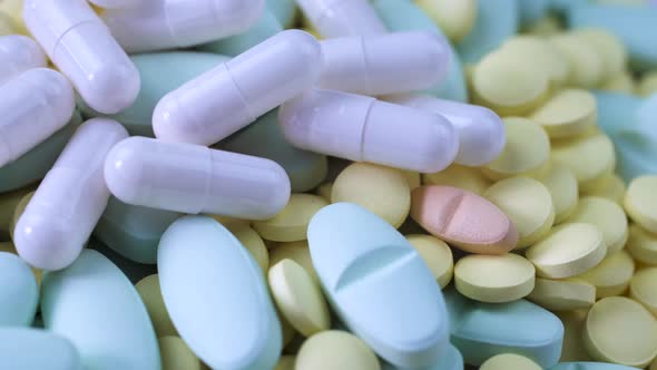 White Capsules Lie on Multi-colored Yellow Blue Pink Pills on a Table Close-up