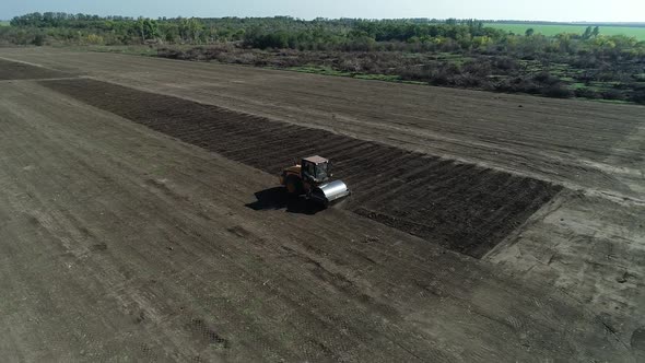 Heavy Roller Compactor is Driving Across the Field Leveling the Soil