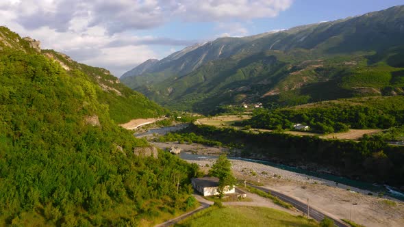 Aerial view of stunning Permet Valley showing dense green mountains, cliffs, river and cloudy sky.