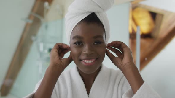 Smiling african american attractive woman putting towel on head and looking at mirror in bathroom