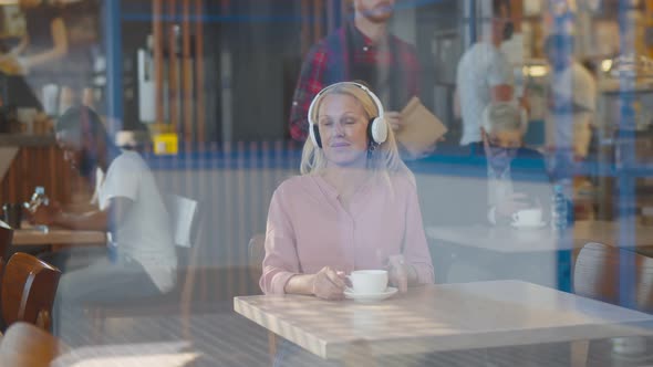 Portrait of Senior Attractive Woman Wearing Headphones Drinking Coffee in Cafe