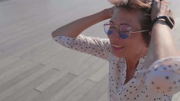 Woman with Colorful Sunglasses Sits on Scene in Urban Park and Enjoys of Bright Sunlight