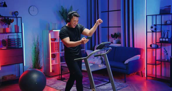 Asian Man in Sportswear Walking on Treadmill and Listening Music in Headphones