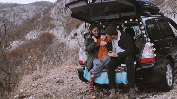 Family  sitting in the open trunk of a black car with baby against the backdrop of autumn mountains