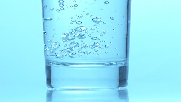 700778 Glass of Sparkling Water against Blue Background, Slow Motion
