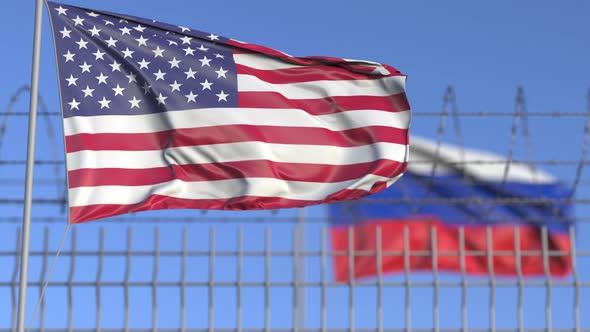 Waving Flags of the USA and Russia Separated By Barbed Wire Fence