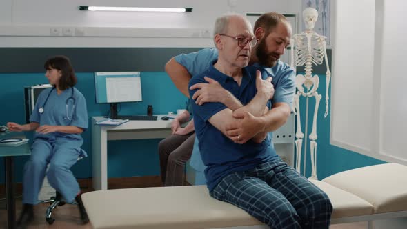 Osteopath Helping Senior Man to Crack Back Bones in Cabinet