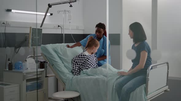 Mother Discussing with Sick Little Daughter While African American Nurse Arrange Bed