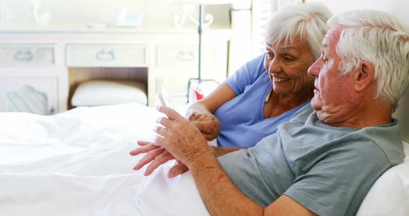 Smiling couple lying on bed and using digital tablet in bedroom