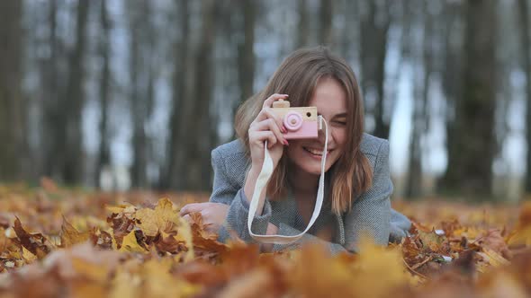 A Young Beautiful Girl Takes Pictures in an Autumn Park Using a Toy Camera