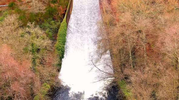 Aerial View Of River Spillway Surrounded By Fall Trees, Tilt Down