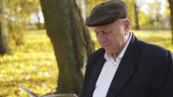 Senior is Surprised and Smiling While Watching Photo Album on Park Bench