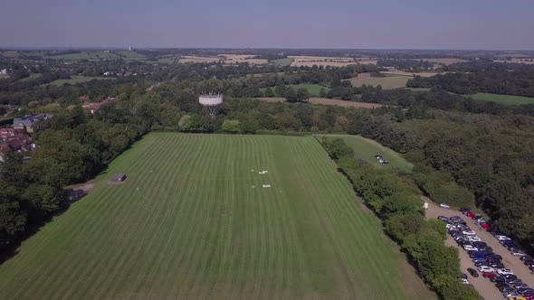 Drone aerial view flying over freshly cut field in Trent Park with car park and water tower in view.