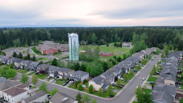 Swiveling drone shot of a water tower nestled between a neighborhood and an elementary school.