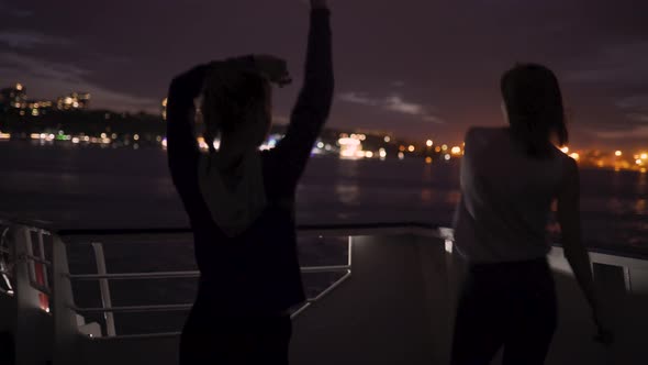 Silhouette of Two Beautiful Young Women Dancing on Ship Deck at Night