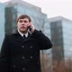 A Businessman on the Street in a Black Coat is Talking on the Phone - VideoHive Item for Sale