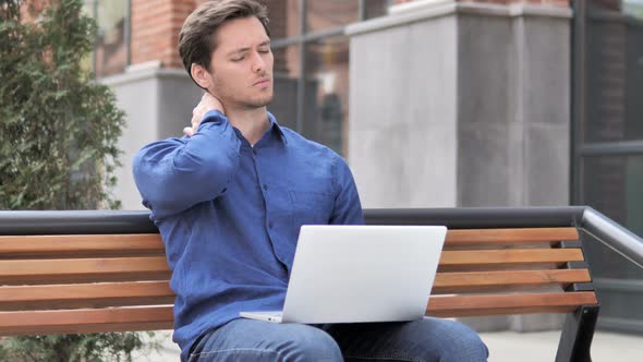 Sitting Outdoor, Young Man with Neck Pain working on Laptop