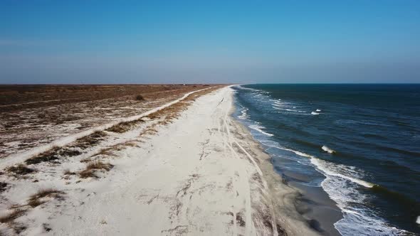 Aerial shot moving backward revealing the seashore with a sandy beach and blue sea with calm waves.