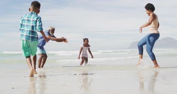 Happy african american couple playing with children on sunny beach