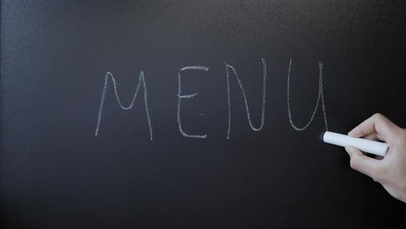 Hand writes word Menu on chalkboard. Menu written on black sign board