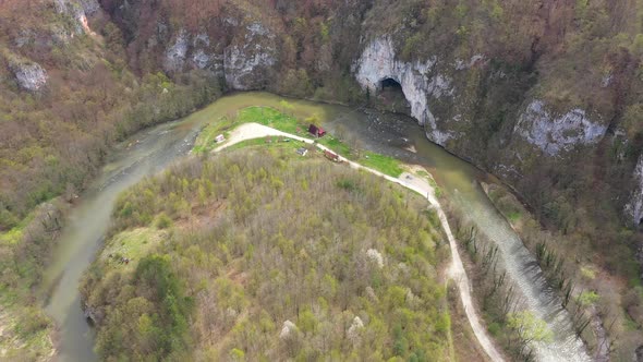 Aerial Above View of a Wild Mountain River Meander and a Gigantic Cave Entrance