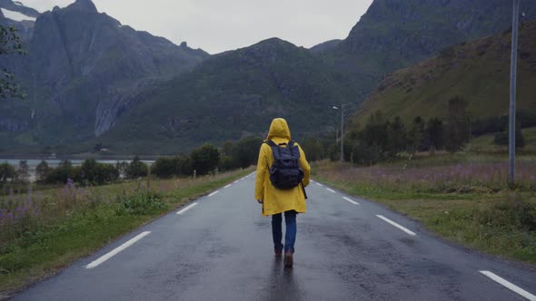 Tourist in raincoat walking on remote road