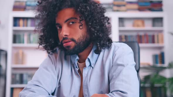 Handsome Arabian Man Smiling at Camera Sits at Table in Library or Cabinet