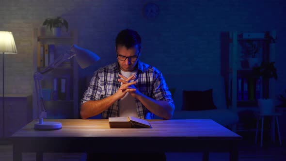 Man Sits at a Table and Reads a Prayer