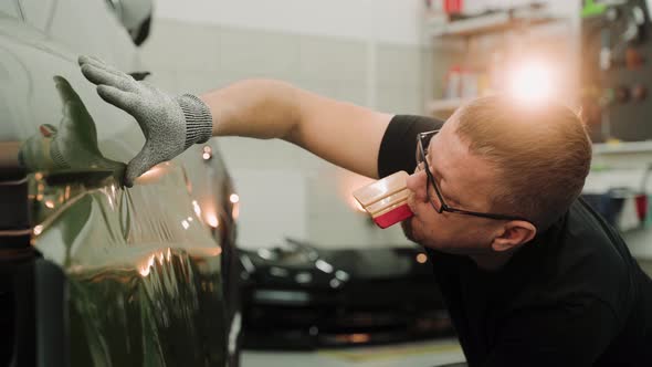 Man Vinyl Wrapping a Car Door in a Work Garage Pulling the Film Down