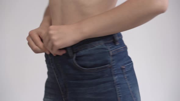 A middle-aged woman who has lost weight measures jeans that have become big.