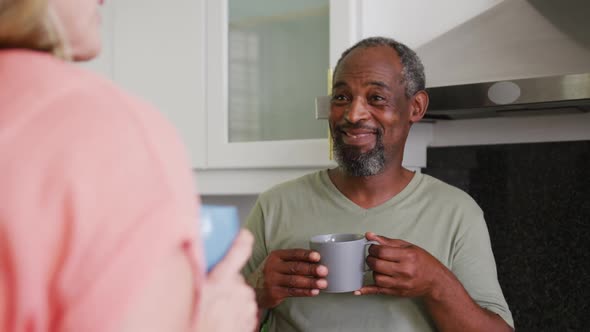 Over shoulder view of diverse senior couple drinking coffee smiling and talking in kitchen