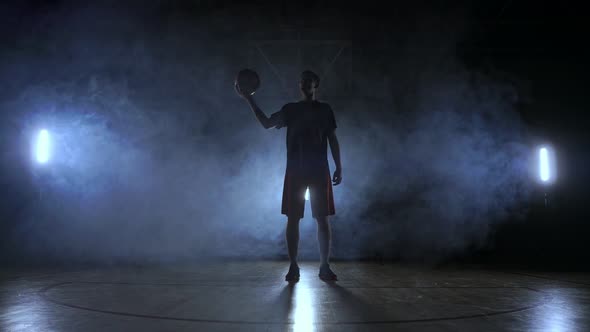 The Silhouette of a Basketball Player on a Dark Background with Smoke on the Basketball Court Throws