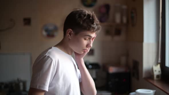 Sleepy teenager comes up to the kitchen in the morning and drinks water